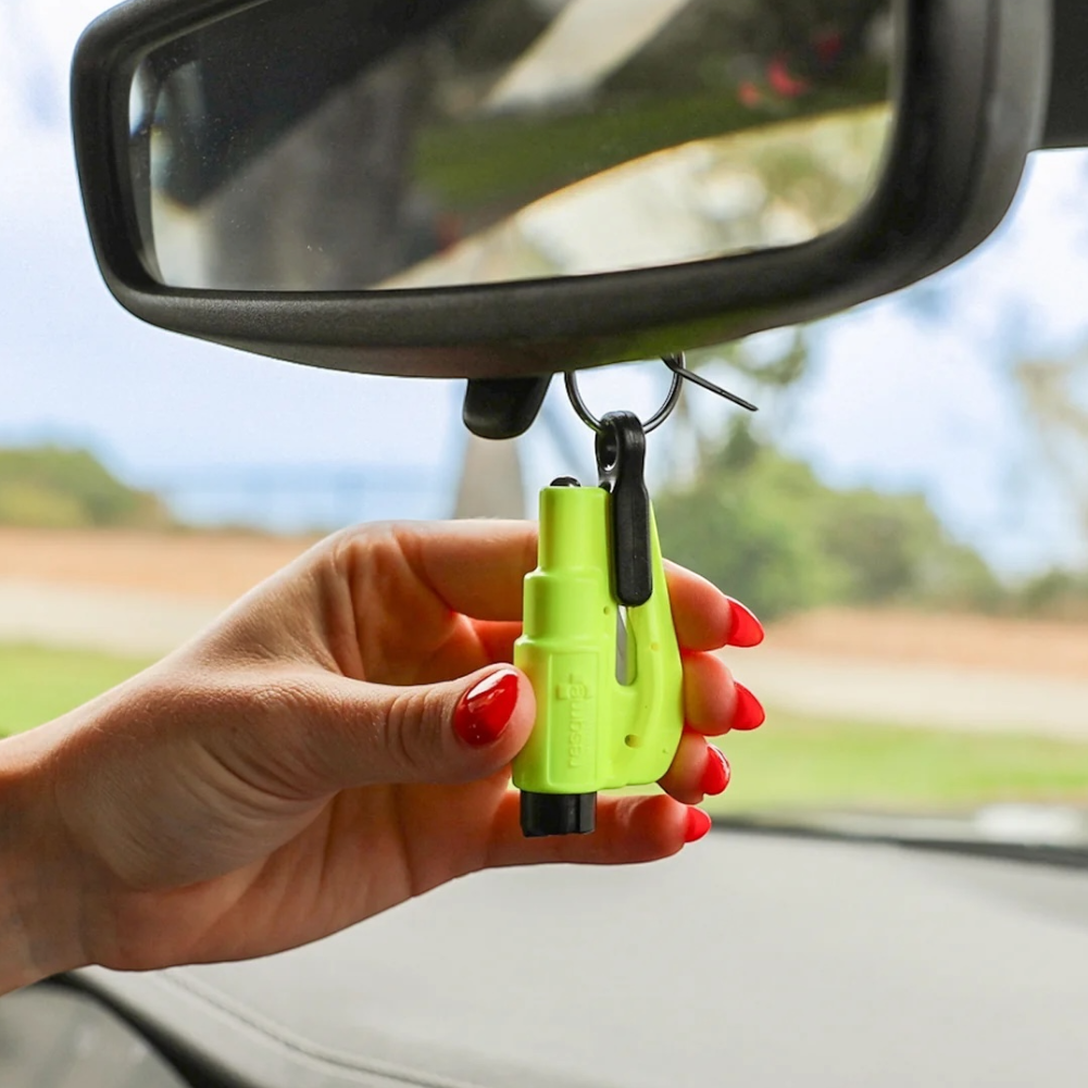 A hand with red nail polish holds a safety yellow ResQMe tool hanging on the rearview mirror. 